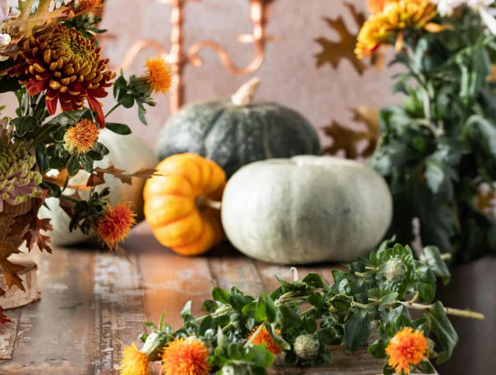 Colorful fall decor with pumpkins and vibrant autumn flowers on a rustic wooden table, perfect for seasonal decorating and creating a cozy home ambiance.